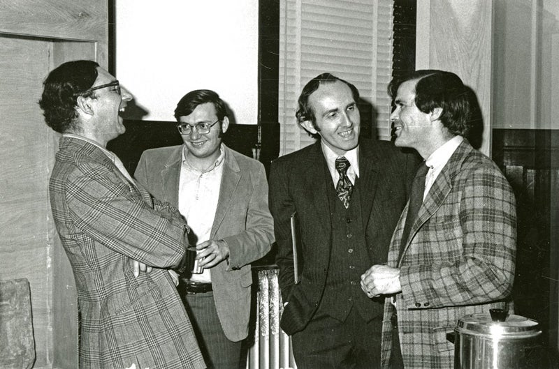 four men in suits laughing.