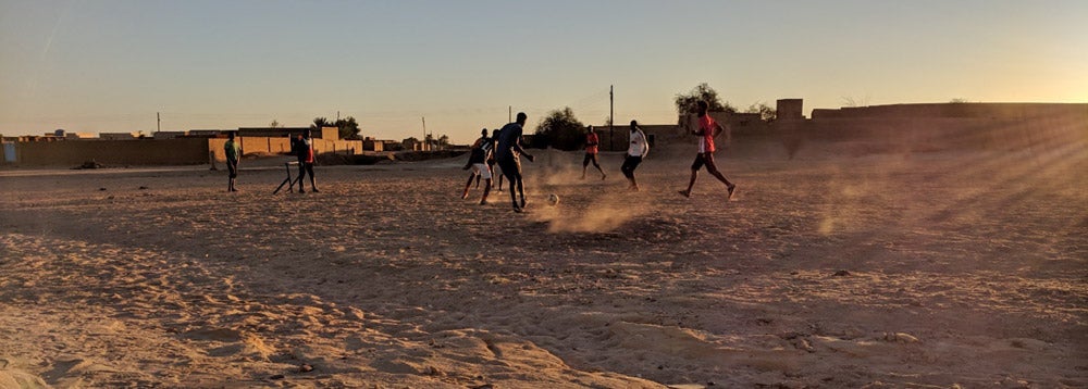 boys playing soccer on a dirt field