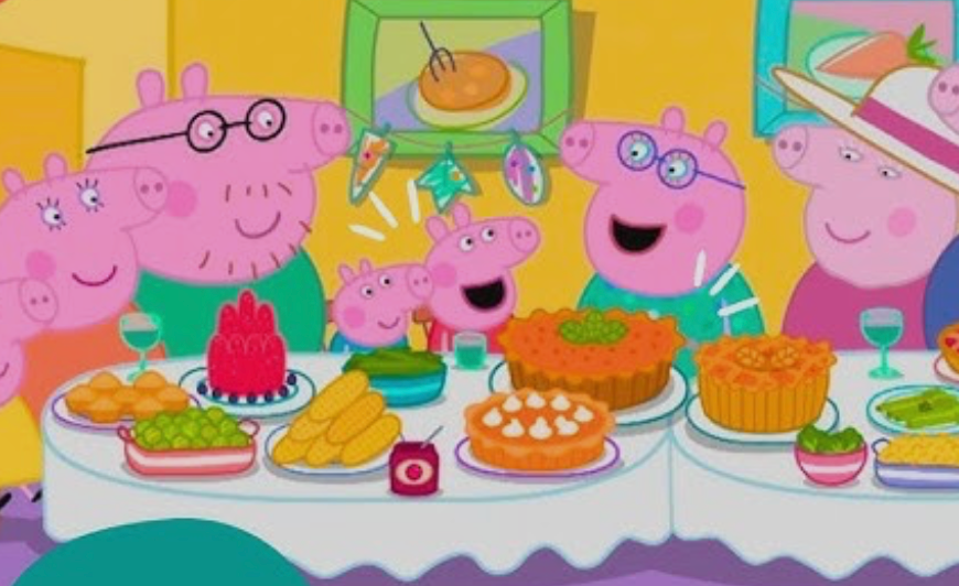 A cartoon pig family sits at a table full of colorful food, smiling and celebrating together. The room is bright and decorated with paintings and a birthday banner.