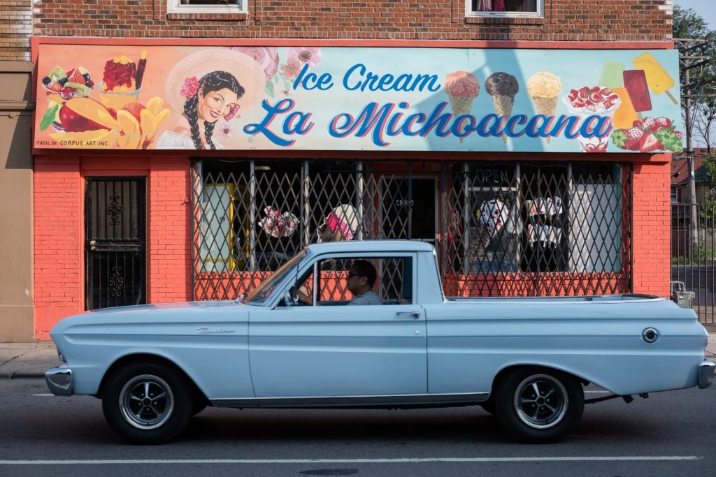 Photograph of man in a car in front of an ice cream store