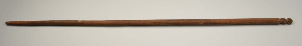 An image of a long wooden staff, with a carving at the top.