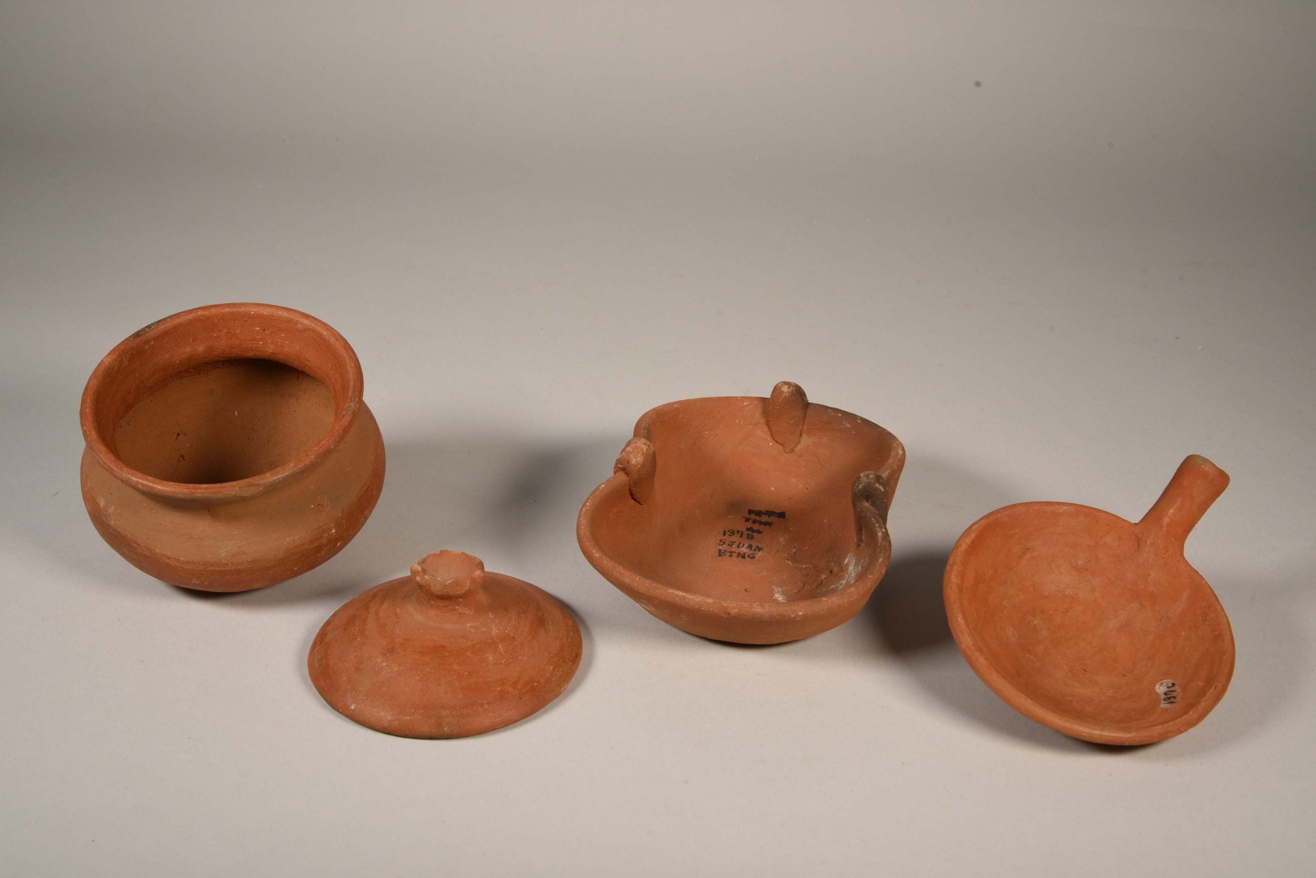 A ceramic pot, pot lid, stove, and frying pan sitting next to each other.