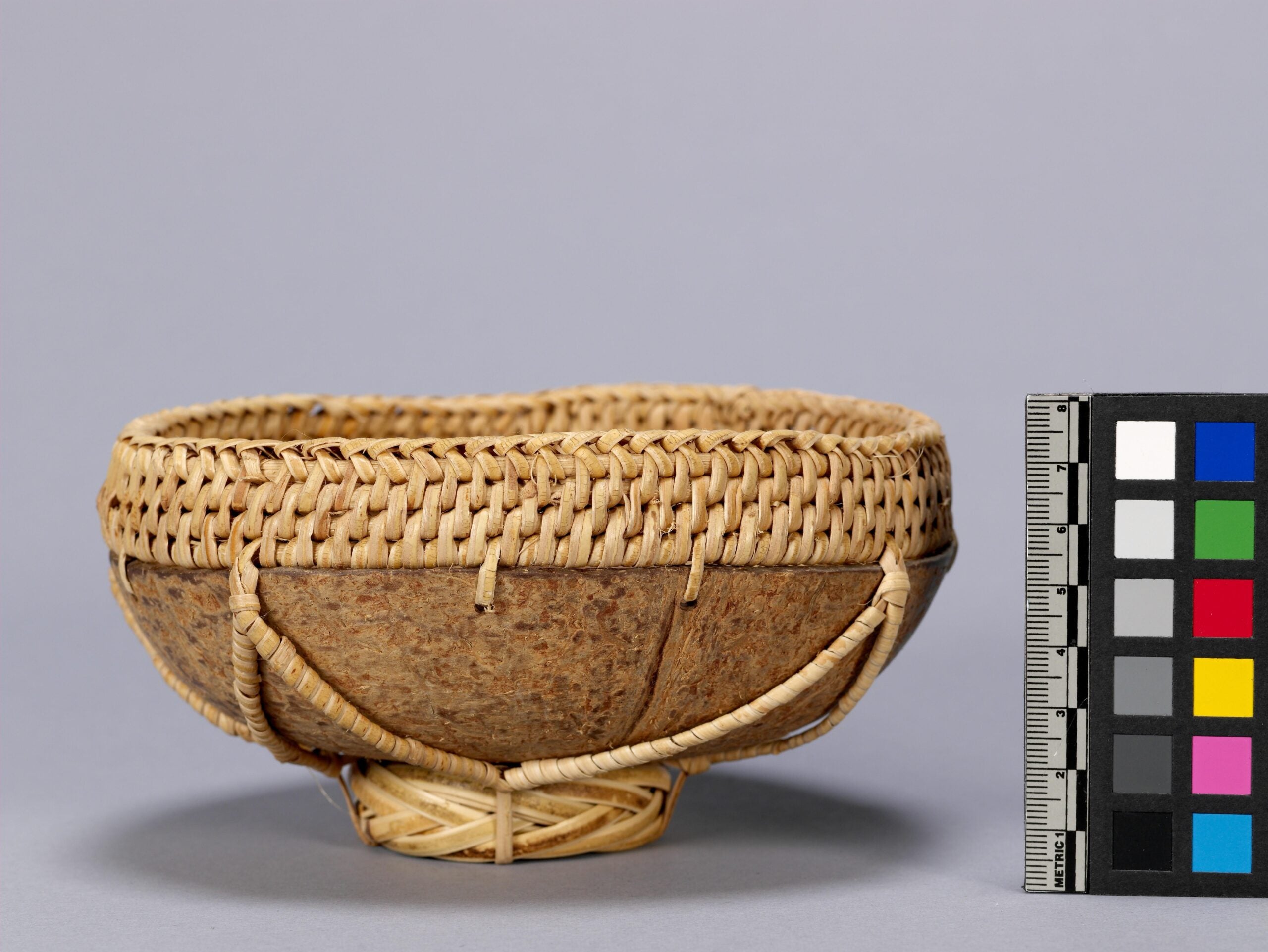 A coconut shell bowl. Intricate weaving line the exterior rim of the bowl and the bottom.