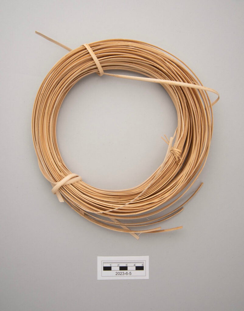This image shows a bundle of split rattan from the Philippines prepared for weaving. The rattan strips are pale tan in color and are coiled into a circular ring. The bundle is secured by several rattan ties that bind the coil together at evenly spaced points. The thin, flexible strips appear smooth and uniform, indicating that they are prepared for use in weaving or basket making.