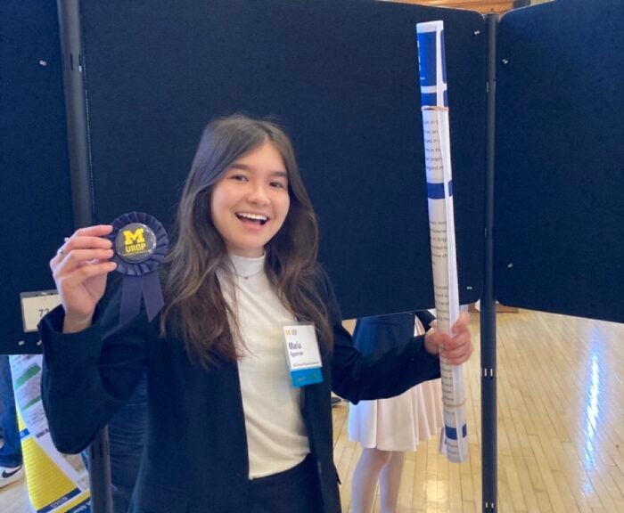 A student holds a blue ribbon and a rolled-up scientific poster