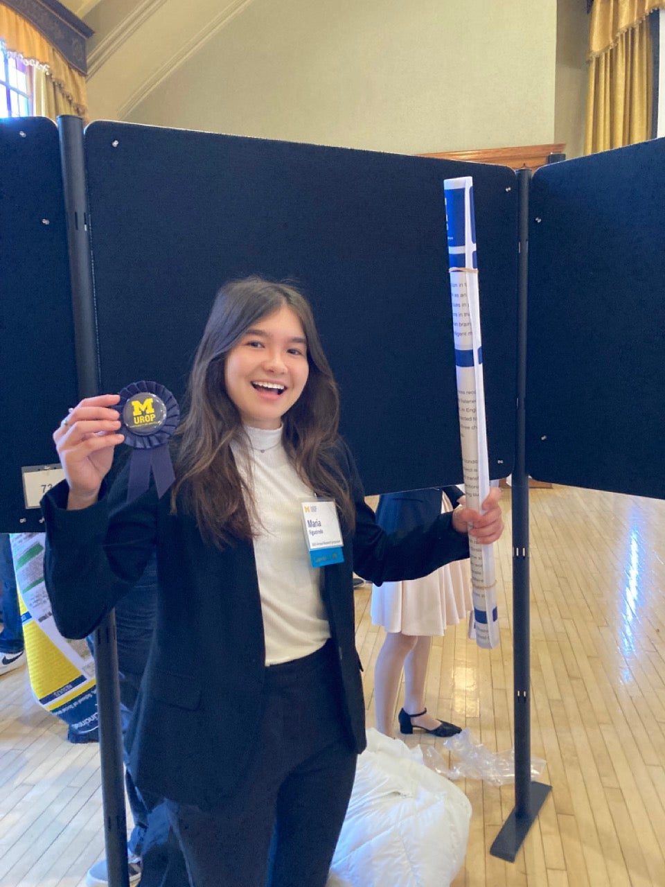 A student poses for the camera with a rolled-up poster and a blue-ribbon award