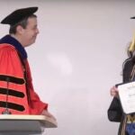 A student receives an award certificate from a professor wearing red academic gowns