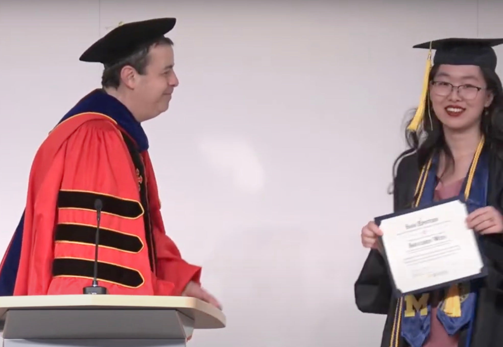A student receives an award certificate from a professor wearing a red academic gown