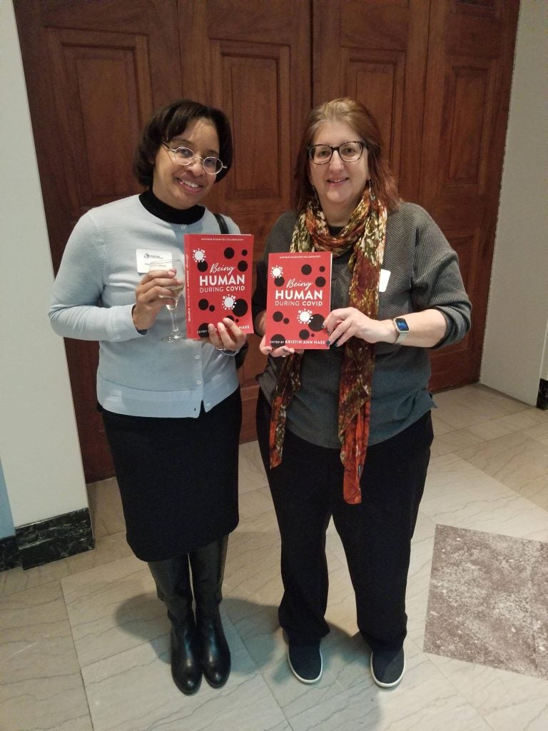 Angela Dillard and Alex Stern smile and hold copies of the book "Being Human During COVID" in the Apse at UMMA.