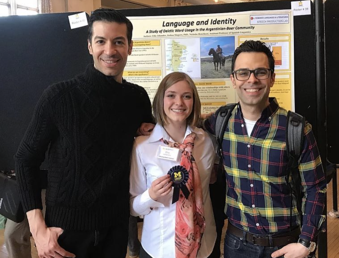 Three individuals pose in front of a poster exhibit; in the middle, Ellie Johandes holds up a U-M UROP ribbon.