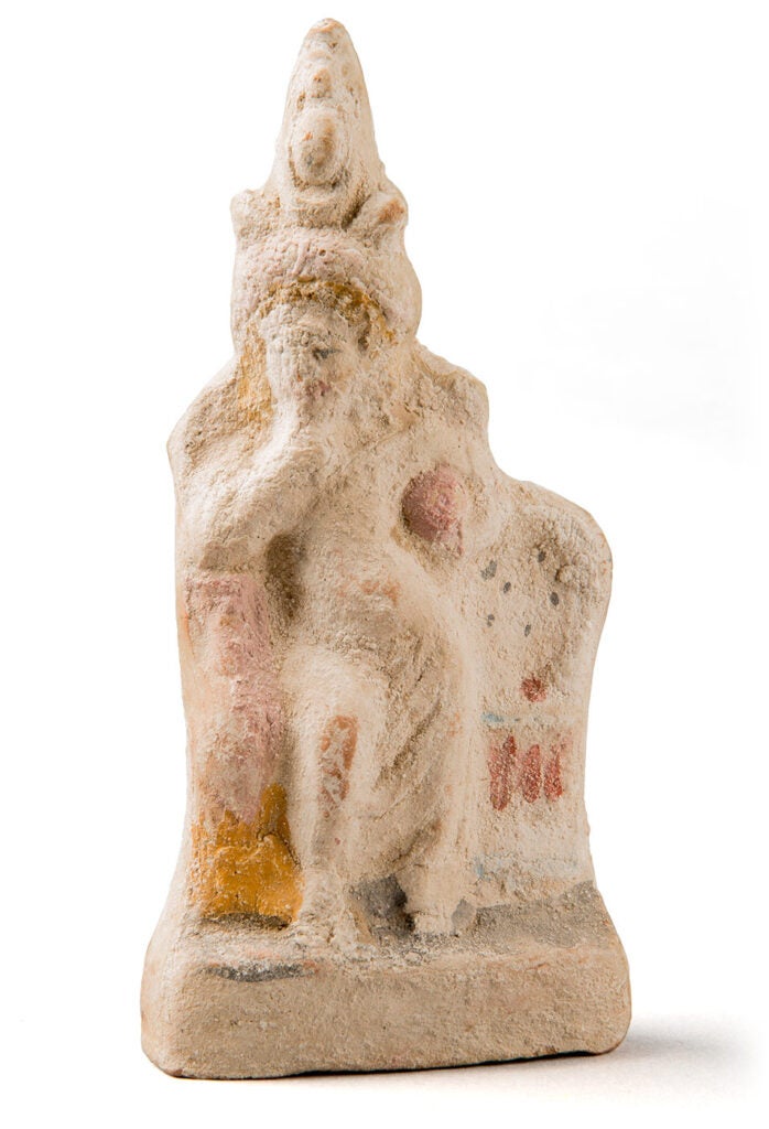 Color photograph of a terracotta statuette of a standing male figure holding a finger to its mouth.