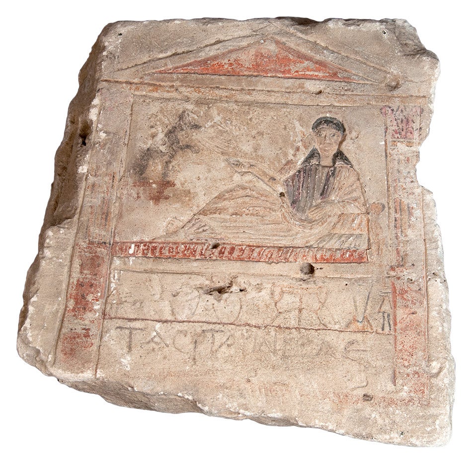 color photograph of a painted limestone grave marker carved with a reclining female figure