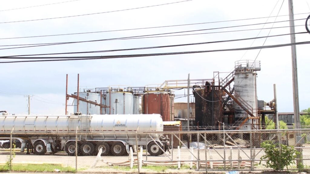 A fenced industrial site with large storage tanks, a tanker truck, and overhead power lines stands on Detroit’s east side. Some tanks at the oil facility appear rusty and weathered, reflecting years of use as discussions around a potential reopening proposal continue.
