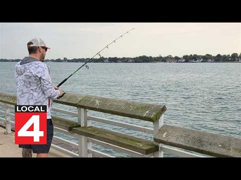 A man stands on a pier fishing in the Detroit River.