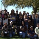 A group of students posing outdoors during a GRCC student field trip, some holding Raiders signs and pennants.