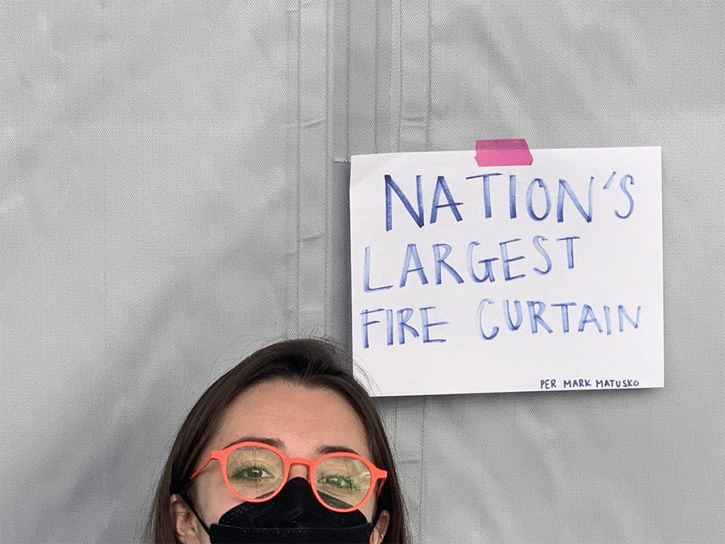 Juanita Pardo Sanchez in front of the smoke curtain and a taped on sign that reads Nation's Largest Fire Curtain per Mark Matusko