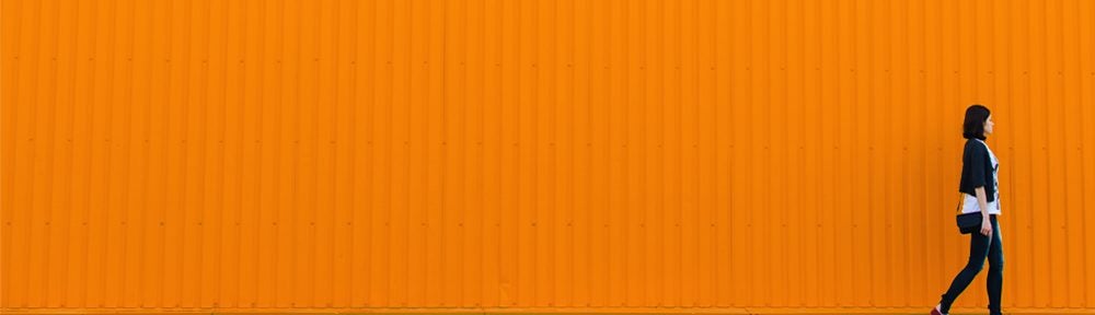 Woman walking in front of a corrugated orange wall