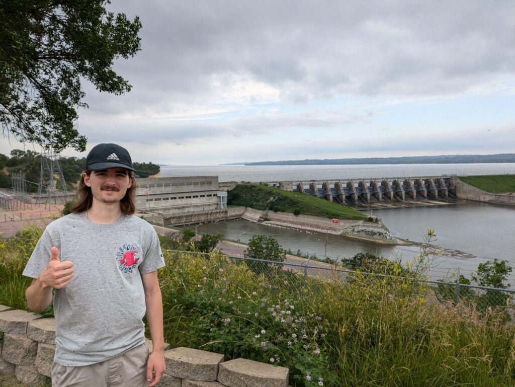 Photo of Colton standing in front of a water treatment plant and dam