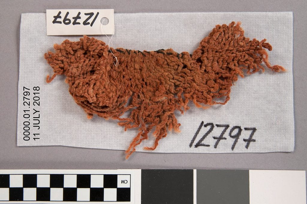 Fragment of a somewhat coarse orange sprang cap with a row of blue/black stitches along one edge.