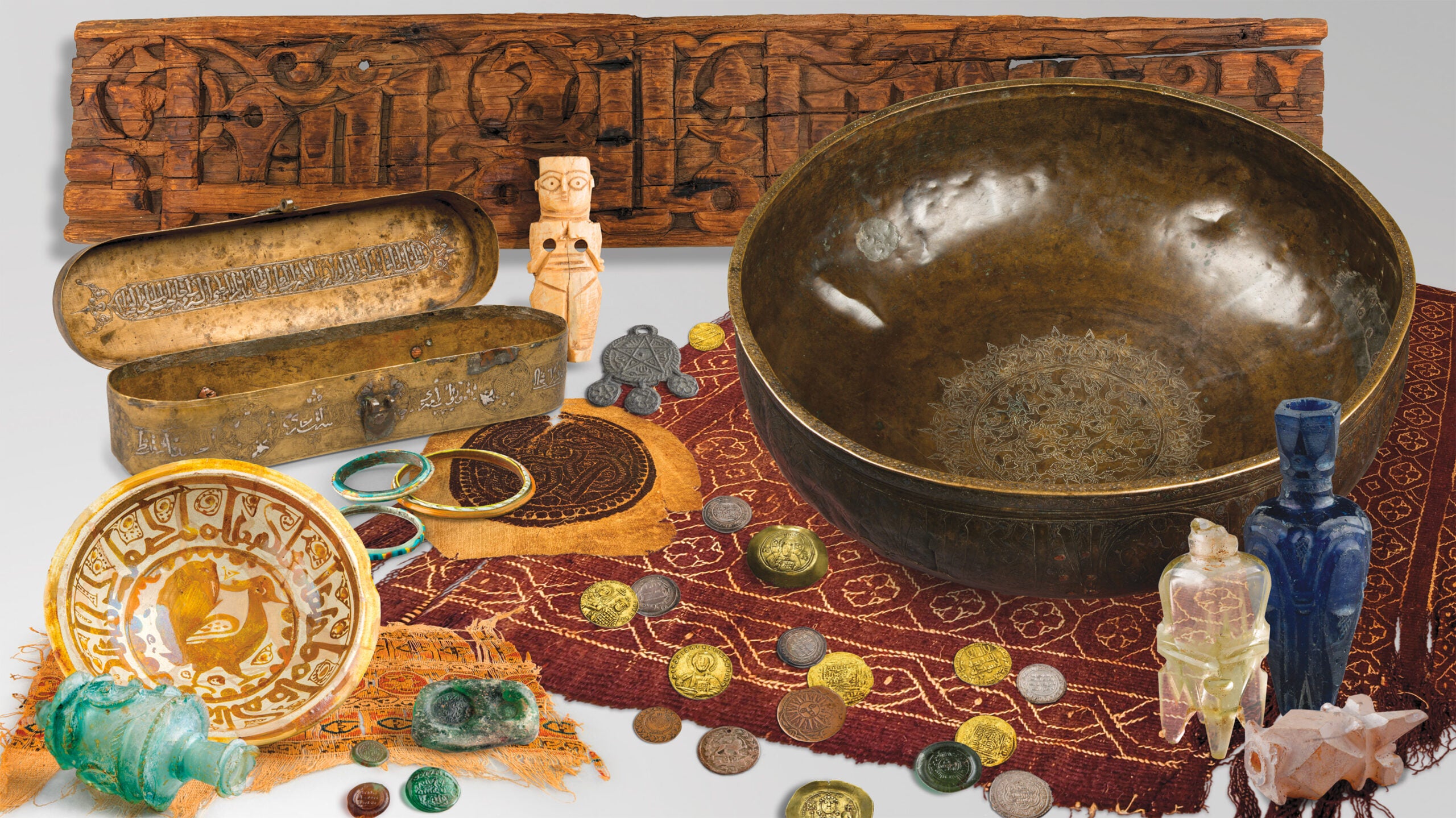 Assemblage of artifacts, including brightly colored textiles, coins, bracelets, amulets, bowls, and flasks.