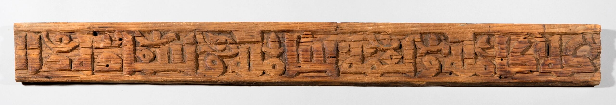 A long, narrow piece of wood with carved writing.