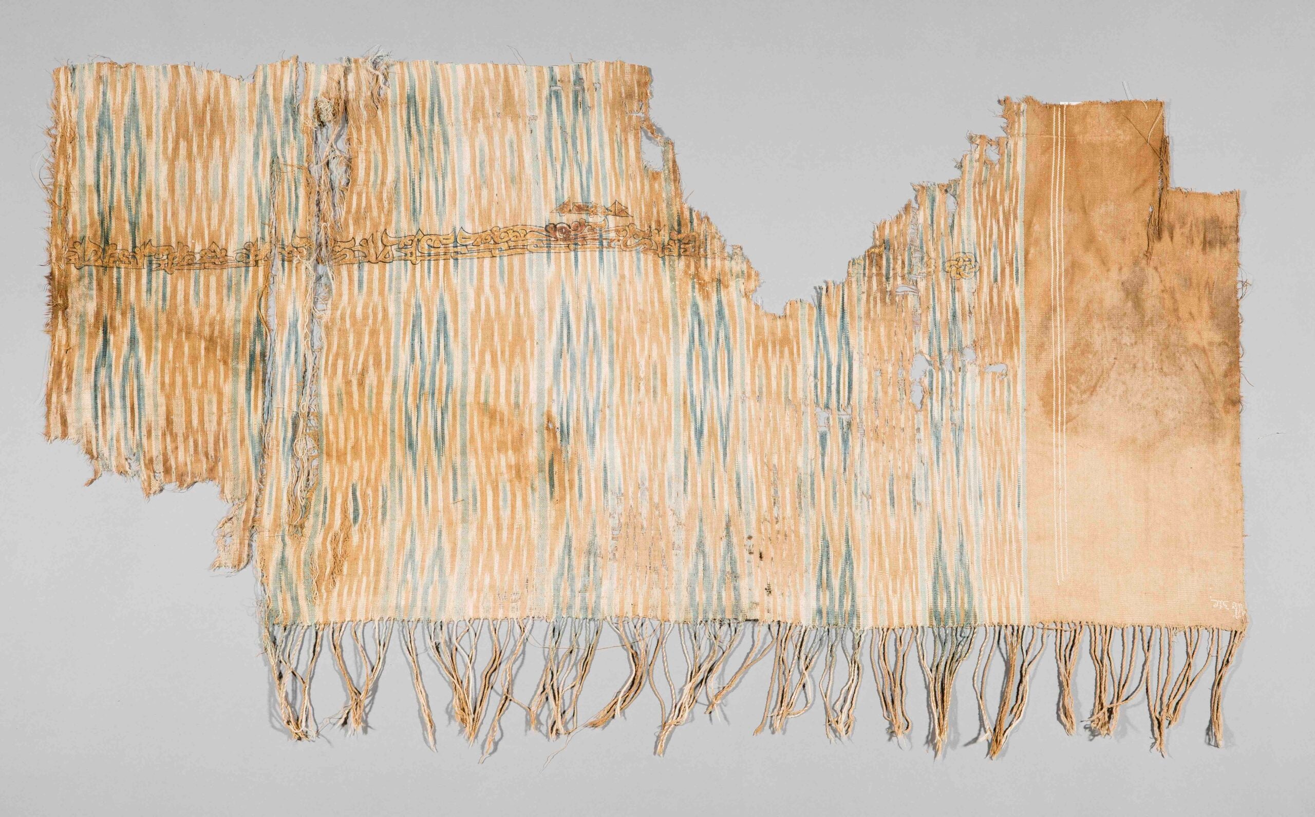 Blue and tan patterned textile with a line of text across the upper portion and fringe along the bottom.