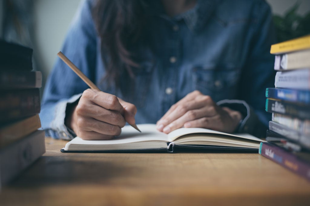Student studying with hand holding a pencil writing on a notebook.