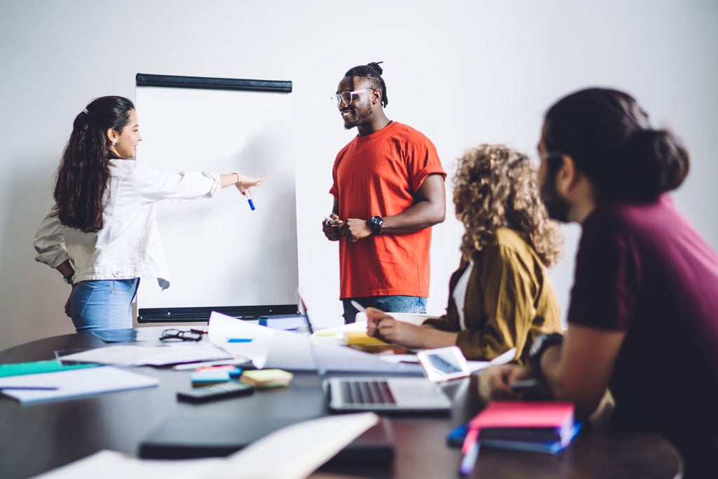 Smiling students standing in front of an easel and giving a presentation in class