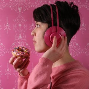 The writer wears headphones and holds a pink donut with sprinkles