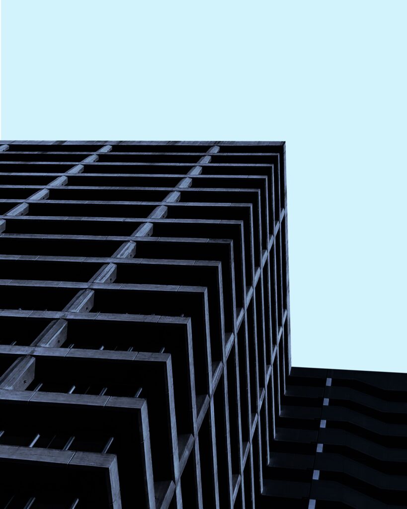 Low-angle view of a modern, geometric building with repeating balcony lines, set against a clear, light blue sky. The structure appears dark and angular.