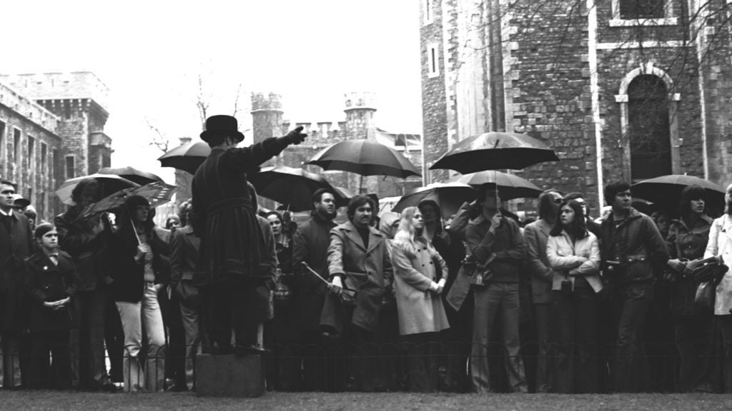 group of people in London listening to a man talk; some are holding umbrellas and others are standing in the rain