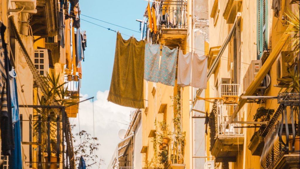 yellowish picture of clothing lines doned with towels hanging across an alley in a european city
