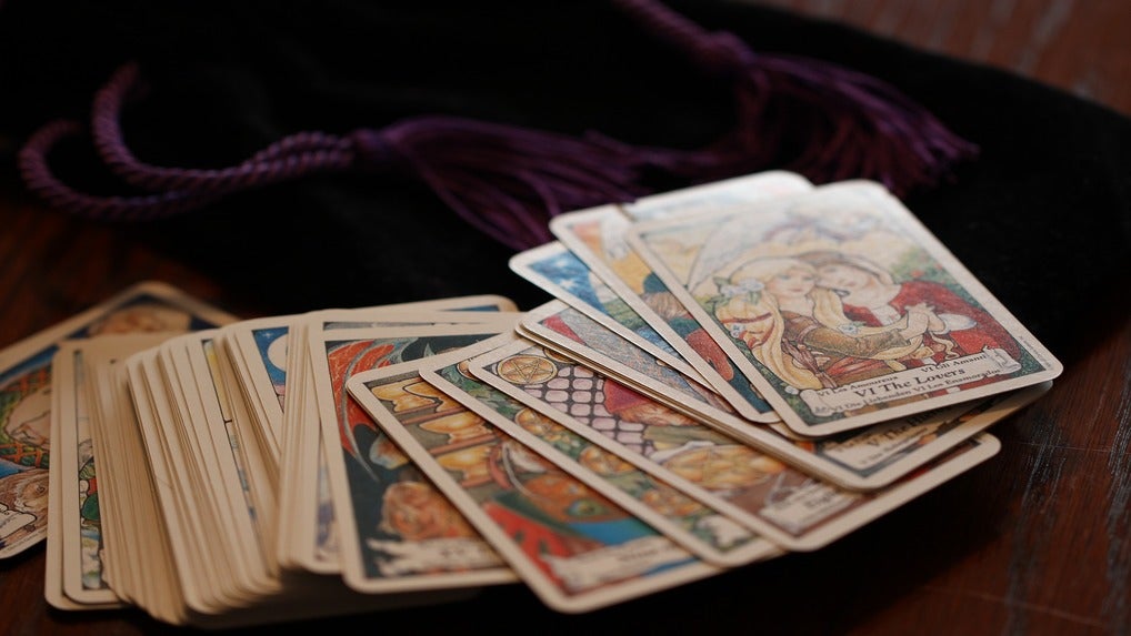 A stack of tarot cards spread across a maroon velvet bag.