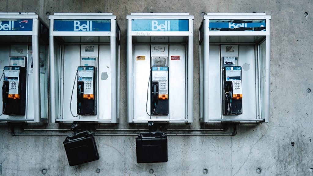 Three Bell phone booths against a concrete wall