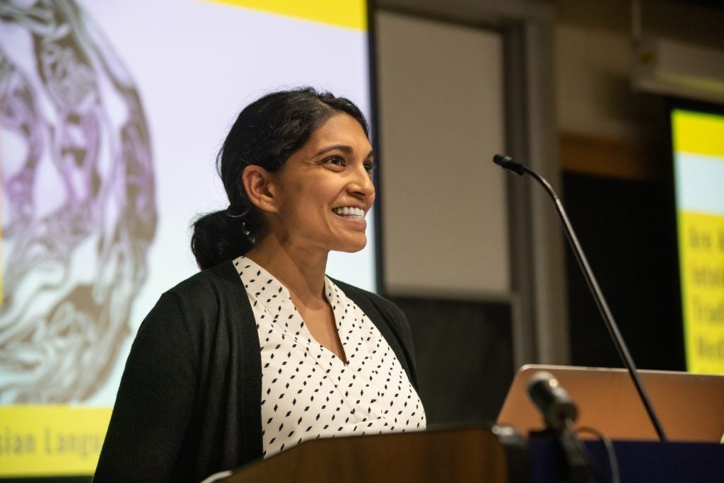 Professor Meha Jain lectures in front of a podium and presentation behind her.
